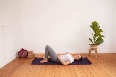 Eine junge Frau führt sanfte Rückbildungsübungen auf einer Matte durch, ihr Baby liegt daneben.