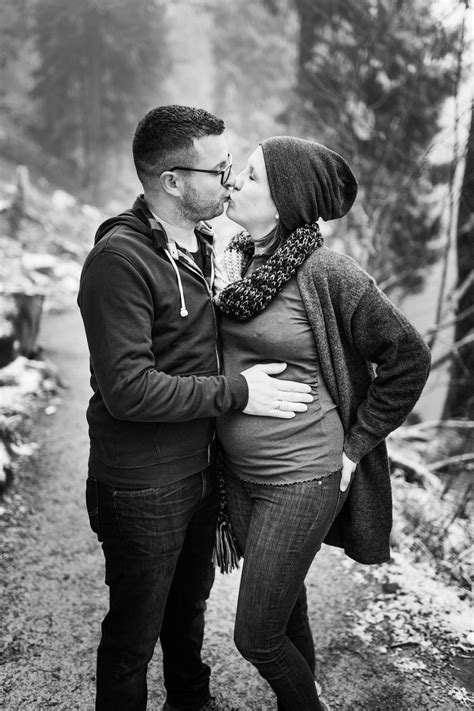 Ein werdendes Elternpaar hält sich liebevoll an den Händen, im Hintergrund unscharf eine Babywiege