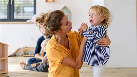 Eine Mutter, die ihr weinendes Kind an der Tür der Kindertagesstätte verabschiedet.