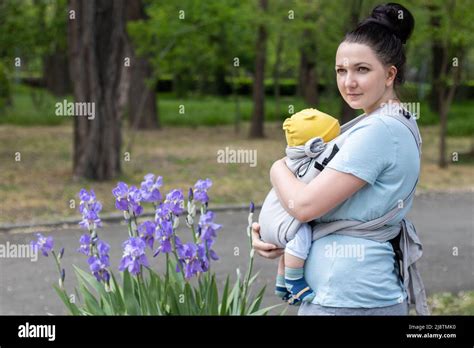 Bild einer Mutter, die ihr Baby liebevoll im Tragetuch trägt, während sie den leeren Kinderwagen schiebt.