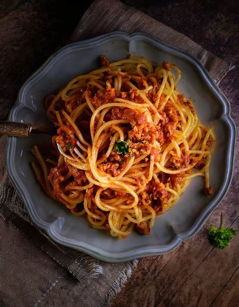 Eine Schüssel mit Babybrei Spaghetti Bolognese, daneben kleine Nudeln und die Zutaten für die Sauce