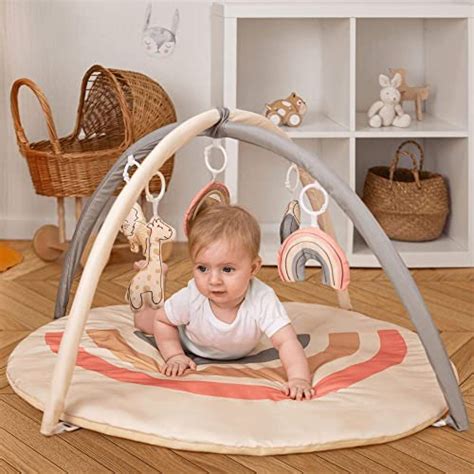 Ein Baby liegt auf einer Krabbeldecke und greift nach bunten Holzspielzeugen, die an einem stabilen Holz-Spielbogen befestigt sind.