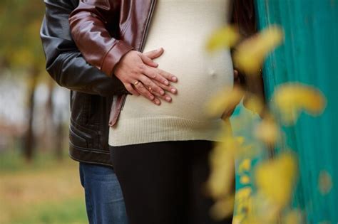 Schwangeres Paar in der Natur, der Mann hält schützend die Hand auf den Bauch der Frau