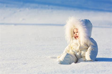 Baby in einem warmen Winteroverall, das draußen im Schnee spielt