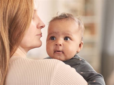 Eine Mutter hält ihr Baby im Arm und blickt es liebevoll an, das Baby schaut interessiert zurück.