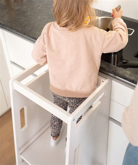 Kind in einem Lernturm, das auf Augenhöhe mit der Arbeitsplatte ist