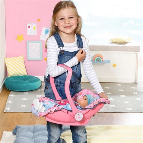 Eine rosa BABY born Babyschale mit verstellbarem Tragegriff und Sicherheitsgurt, daneben eine BABY born Puppe im passenden Alter.