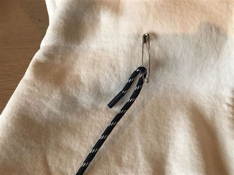 Detailaufnahme, wie eine Kordel mit einer Sicherheitsnadel durch den Tunnelzug eines Spielzeugsacks gefädelt wird