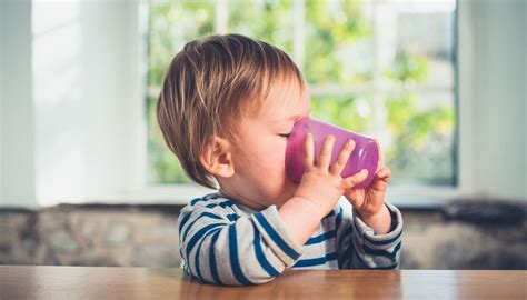 Ein Baby versucht, aus einem kleinen Becher zu trinken, wobei etwas Wasser daneben tropft.