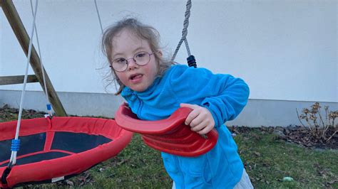 Ein Kind mit Down-Syndrom lacht auf einer Nestschaukel.