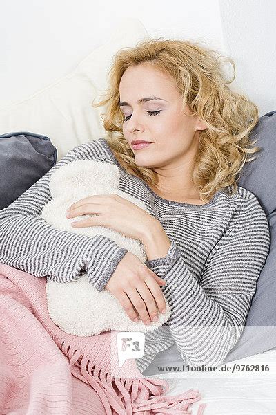 Frau in entspannter Position auf einer Couch liegend, mit einer Wärmflasche auf dem Bauch