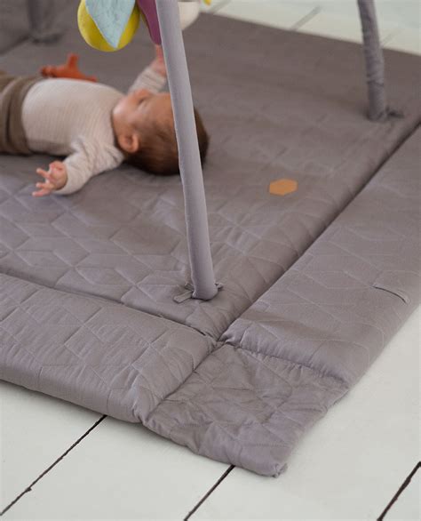 Abbildung eines Babys, das auf einer bunten Krabbeldecke mit Spielbogen spielt